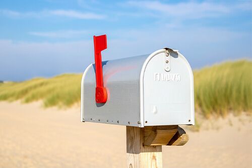 Briefkasten mit roter Fahne nach oben an einem Strand mit Düne im Hintergrund