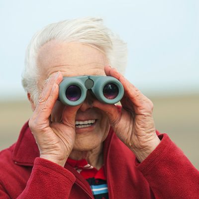 Ältere Person hält ein Fernglas vor die Augen.