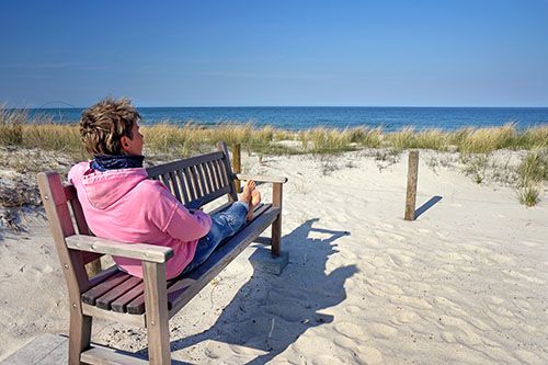 Eine Frau auf einer Bank blickt über Deich, Strand und Nordsee.