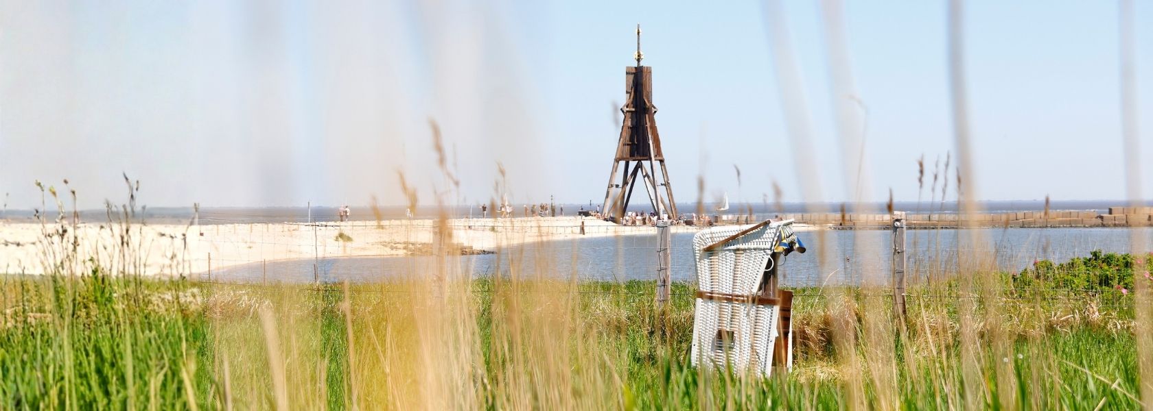 Die Kugelbake am Cuxhavener Strand und ein Strandkorb, durch Schilf-Halme fotografiert.