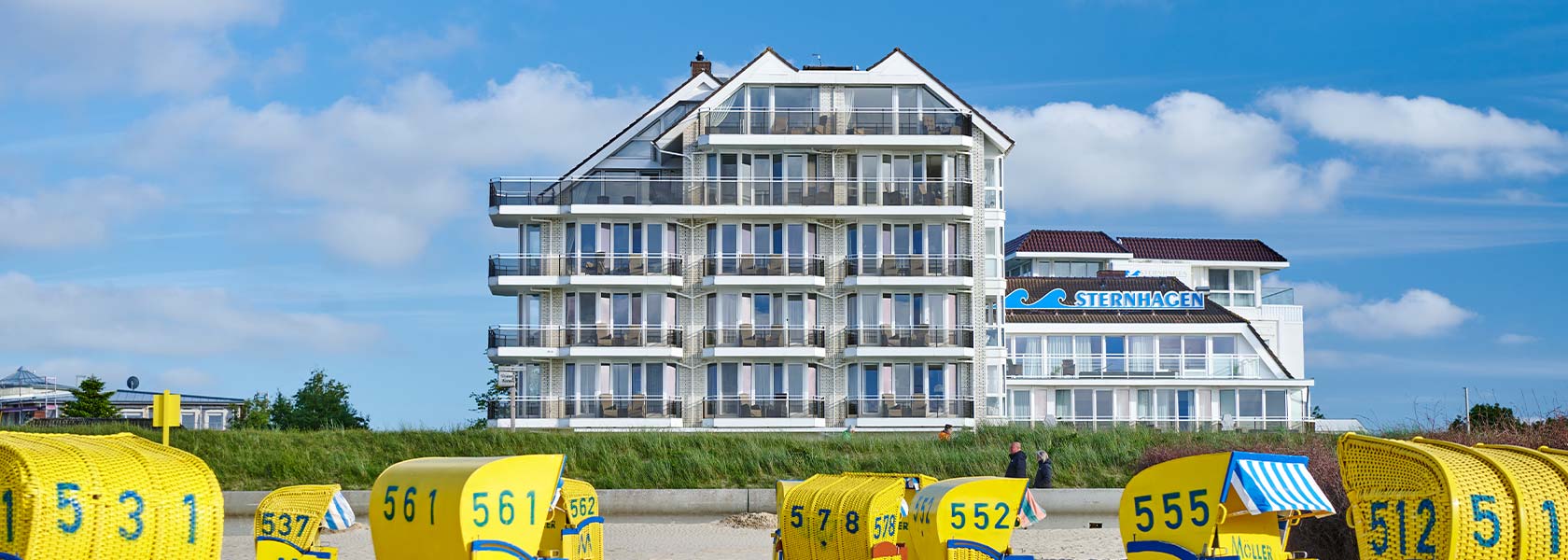 Das Badhotel Sternhagen mit gelben Strandkörben am Strand im Vordergrund
