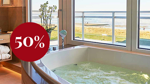 Das Foto ist von einem der Bäder in einer der Suiten des Badhotels. Eine Badewanne an einer Fensterfront, die zum Strand gerichtet ist, ist halb angeschnitten auf dem Foto. Ein roter Kreis ist auf dem Bild und es steht 50 % drin.